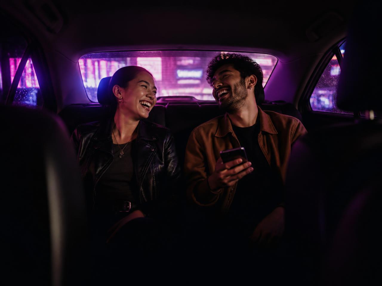 Two riders laughing in the back seat of a car lit by purple city neon